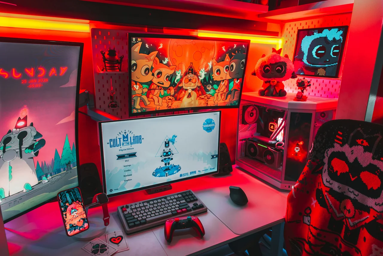 Estação de jogos com monitores, teclado, controle e computador iluminados em vermelho.