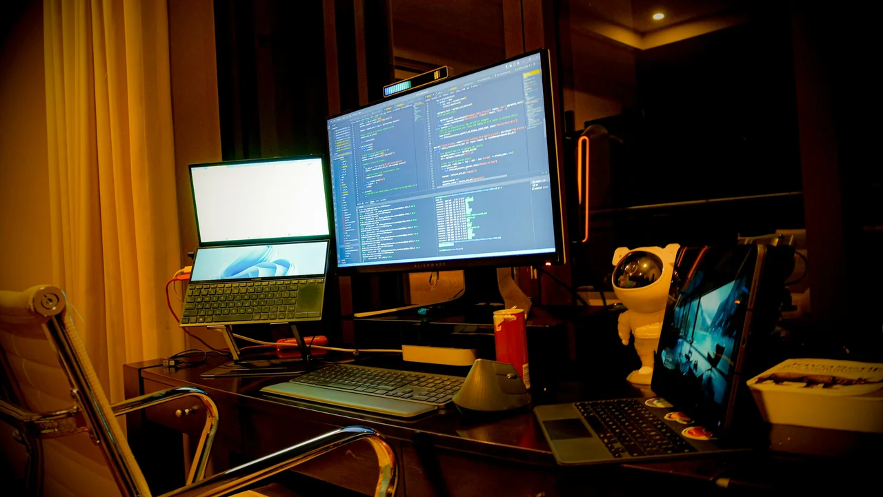 Estação de desenvolvimento com dois monitores e um notebook sobre a mesa.